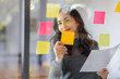 © David - Business female employee with many conflicting priorities arranging sticky notes commenting and brainstorming on work priorities colleague in a modern office.