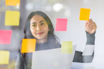 Business female employee with many conflicting priorities arranging sticky notes commenting and brainstorming on work priorities colleague in a modern office.