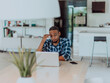 © .shock - African American man in glasses sitting at a table in a modern living room, using a laptop for business video chat, conversation with friends and entertainment