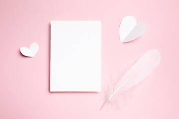 Valentine Day letter or card mockup with white feather and paper heart on light pink background, top view, flat lay. Blank wedding invitation, empty holiday greeting card mockup