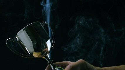Wall Mural - male hand holding silver trophy on black background with smoke