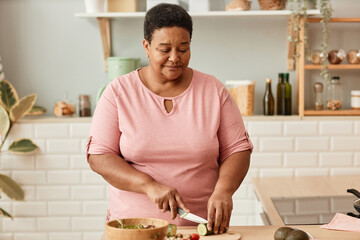 Waist up portrait of senior black woman cutting vegetables while cooking in cozy home kitchen,copy space