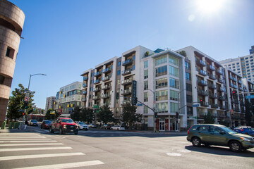 Wall Mural - an intersection at Grand Ave and Olympic Blvd with a white and brown apartment building, cars driving and people walking with a clear blue sky in Los Angeles California USA