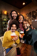 Vertical portrait of a Portrait of A group of friends looking at camera in the restaurant bar after work at the pub happy hour. Happy friends having fun together drinking alcohol indoors.