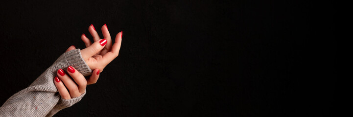 Wall Mural - Female hands in gray knitted sweater with beautiful manicure - red nails on dark black background with copy space banner. Wide panoramic header