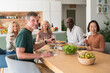 © PhotoAlto - Group of diverse senior friends gathered together for lunch in the kitchen