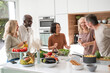 © PhotoAlto - Group of diverse middle-aged friends getting together for dinner chatting in kitchen while cooking