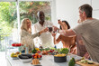 © PhotoAlto - Diverse group of senior friends making a toast while gathered around kitchen island