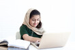 Adorable Pakistani Muslim girl with beautiful eyes wearing hijab, studying online, doing homework by using laptop computer, student kid reading book on white background.