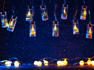 Sticker - Christmas garland background, glowing light bulbs on a blue background, copy space, falling snow