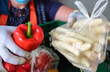 Lebensmittelspende Tafel: Frau mit Handschuhen packt Obst und Gemüse wie frische Paprika in grüne Kisten für die Verteilung an Bedürftige - selektiver Fokus