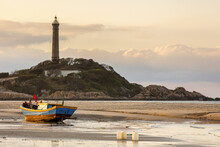 Colourful Fishing Boat Tied To The Beach And A Lighthouse On A Hill Along The Coast, Ke Ga Cape; Ke Ga, Vietnam