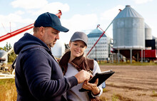 Mature Couple Working On Their Farm, Standing In Front Of Their Grainery While Consulting Tablet Computer; Alcomdale, Alberta, Canada