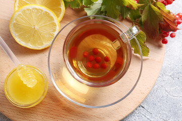 Wall Mural - Cup of delicious tea with lemon, honey and viburnum on light grey table, flat lay