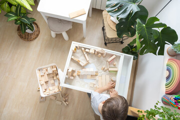 Cute boy kid playing sensory box kinetic sand table with Montessori wooden materials. Top view.