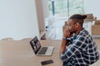 © .shock - African American man in glasses sitting at a table in a modern living room, using a laptop for business video chat, conversation with friends and entertainment