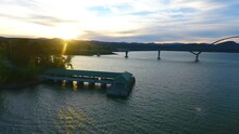 Aerial Pan Of Tower And Docks With Bridge Connecting New York To Vermont And Sun Setting Behind Mountains