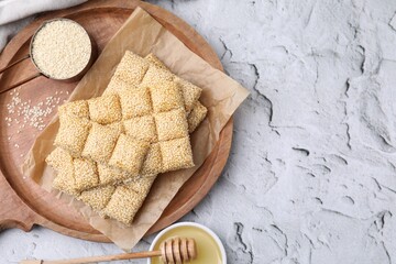 Wooden tray with delicious sweet kozinaki bars, sesame seeds and honey on white textured table, flat lay. Space for text