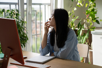 Procrastination in online learning. Dreamy Asian student girl getting distracted while studying remotely at home, sitting at desk with computer looking out window, having no motivation to study