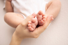 Children's Foot In The Hands Of Mother, Father, Parents. Feet Of A Tiny Newborn Close Up. Little Baby Legs. Mom And Her Child. Happy Family Concept. Beautiful Concept Image Of Motherhood Stock Photo. 