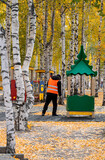 Fototapeta Dmuchawce - A man sweeps yellow leaves in an autumn park on a playground