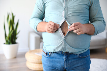 Young overweight man in tight shirt at home, closeup