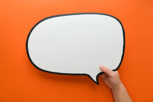 Speech Bubble In Hand On An Orange Background. Comic Cloud With A Place For Text