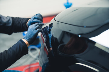 Wall Mural - Car detailing - lights tinting. Unrecognizable hands of professional expert in protective gloves on hands applying a thin laminate film. High quality photo