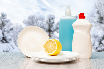 Bottles of dishwashing liquid, plates and lemon with winter on background.