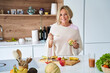 © PhotoAlto - Attractive senior lady enjoying her fruit salad in kitchen