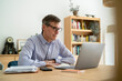 © PhotoAlto - Senior businessman sitting at desk while using laptop