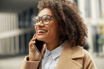 Wall Mural - Close up of afro american woman wearing glasses talking phone with friends during city walking