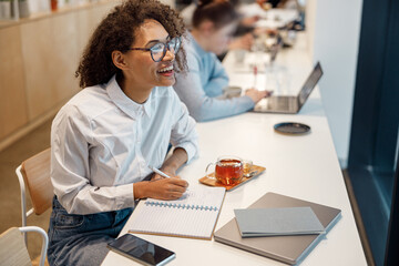 Wall Mural - Smiling woman freelancer working laptop and making notes while sitting in cozy coworking