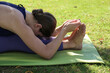 Young woman practicing yoga in the park. Fit yogini doing a seated forward bend on a green mat outdoors. Close up, copy space, background.