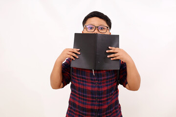 Wall Mural - Shocked asian school boy standing while covering part of the face with his book. Isolated on white background