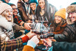 © Davide Angelini - Happy multiracial friends toasting red wine at restaurant terrace - Group of young people wearing winter clothes having fun at outdoors wine bar table
