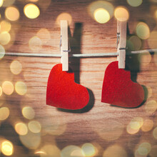 Two Red Hearts On Clothespins On Wooden Background. Beautiful Bokeh Effect From A Garland.
