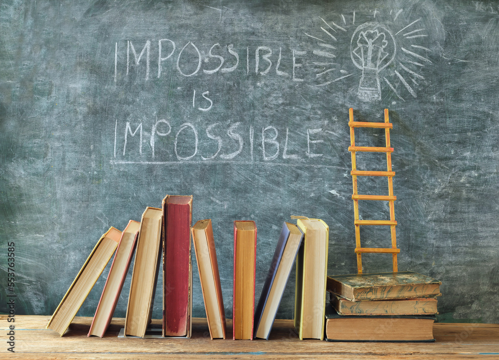 Stack of hardback books with slogan impossible is impossible on blackboard.Learning,education,development, ladder of sucess and back to school concept.
