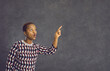 Young beautiful african american woman in casual clothes with surprised facial expression pointing finger aside. Woman stands on a gray background and points to the free space for text. Banner.