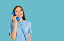 Hotline Service. Joyful Beautiful Young Woman Talking On Retro Telephone, Isolated On Light Blue Background. Happy Woman With Blue Wired Phone Handset Near Copy Space. Telephone Communication Concept.