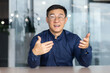 © Liubomir - Video call online meeting asian businessman looking web camera and having fun talking and gesturing, man working inside office sharing plans with partners and colleagues, boss in shirt and glasses.