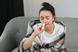Nasal spray in hand of sick young woman sitting on couch. Allergic rhinitis symptoms and treatment