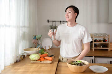 Wall Mural - An Asian young man drinking fresh water in kitchen at home , healthy lifestyle concept