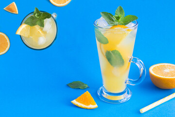 Wall Mural - Orange drink or lemonade with mint and ice in the drinking glass on the blue background. Close-up. Copy space.