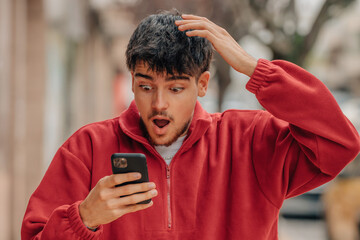 Wall Mural - young man with mobile phone in the street with surprised expression