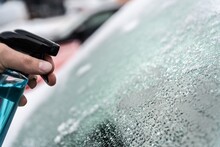 Man uses a bottle of de-icer to defrost the ice-covered windshield of his car