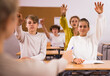 Teenage schoolboys and schoolgirls sitting with hands raised during lesson at secondary school