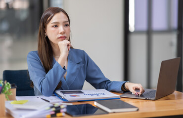 Portrait of tired young business Asian woman work with documents tax laptop computer in office. Sad, unhappy, Worried, Depression, or employee life stress concept	