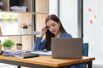 Portrait of tired young business Asian woman work with documents tax laptop computer in office. Sad, unhappy, Worried, Depression, or employee life stress concept	