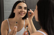 © New Africa - Young woman applying oil onto eyelashes near mirror indoors